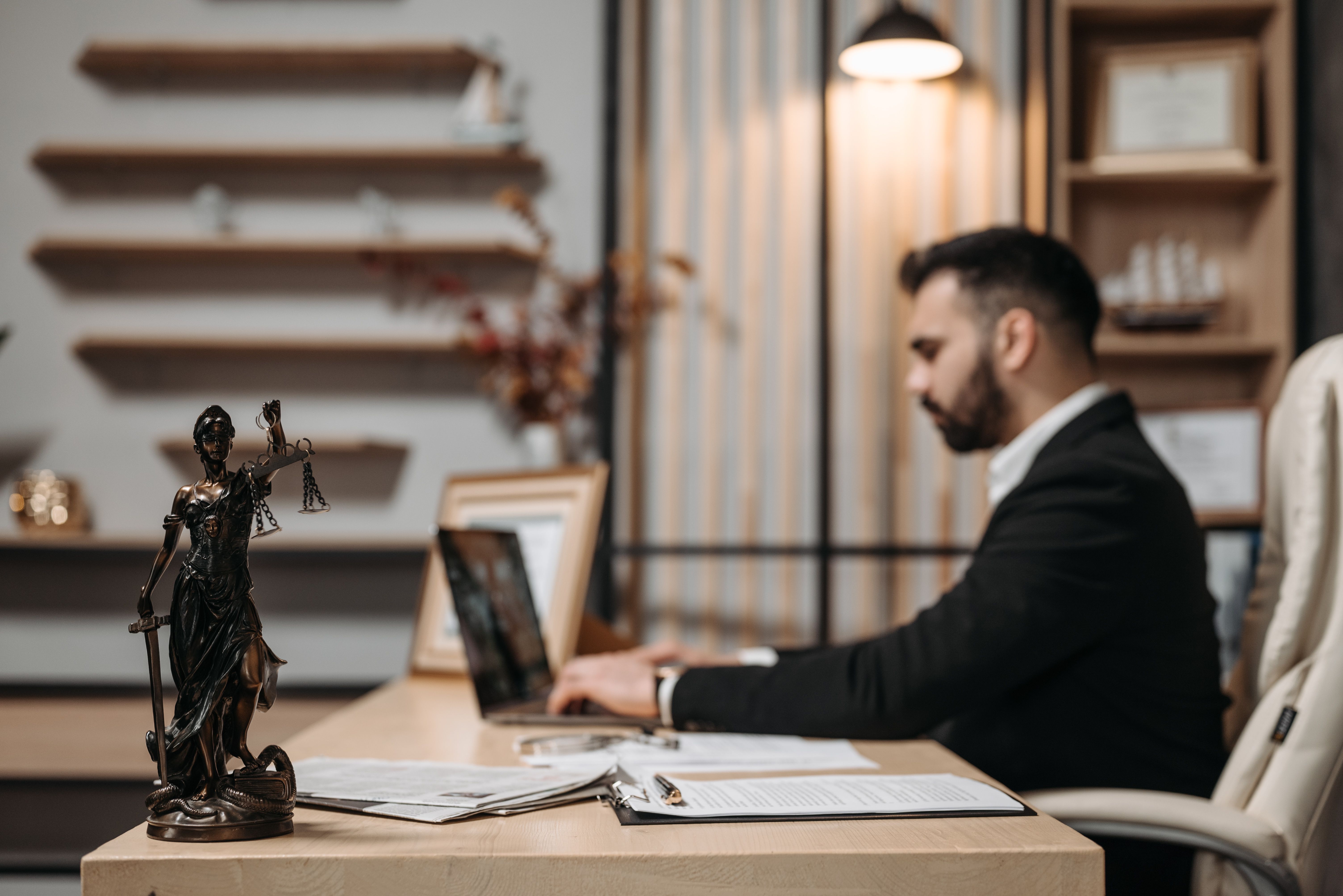 Lawyer reviewing legal documents on a laptop in a modern office with Lady Justice statue